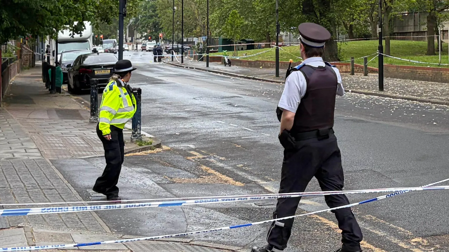  Two police officers stand by the side of a section of the road which has been cordoned off