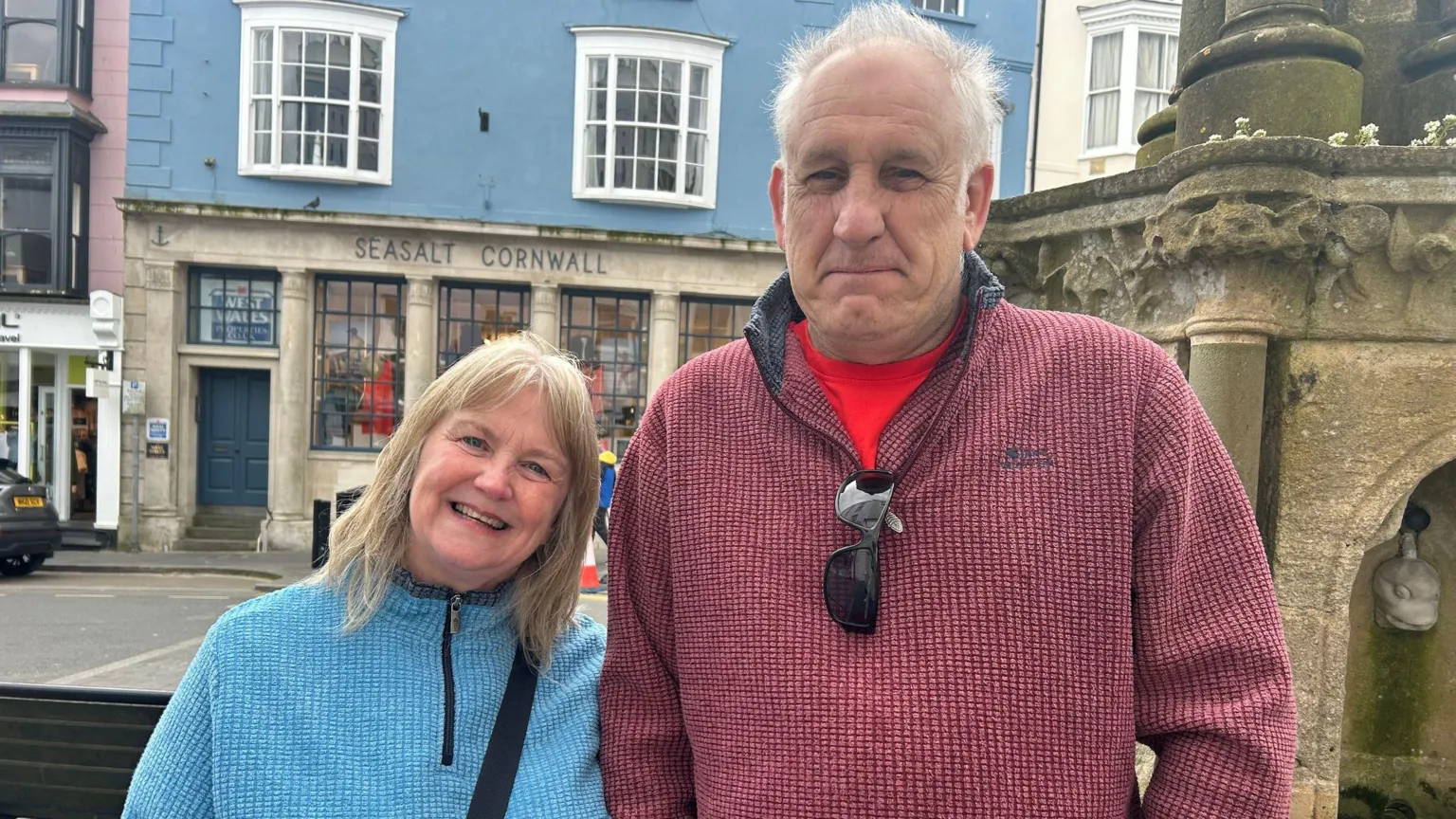  Julie Robinson in a blue jumper and Paul Wiston in a red jumper and red t-shirt with sunglasses hooked on his collar. Standing outside a Seasalt Cornwall shop.