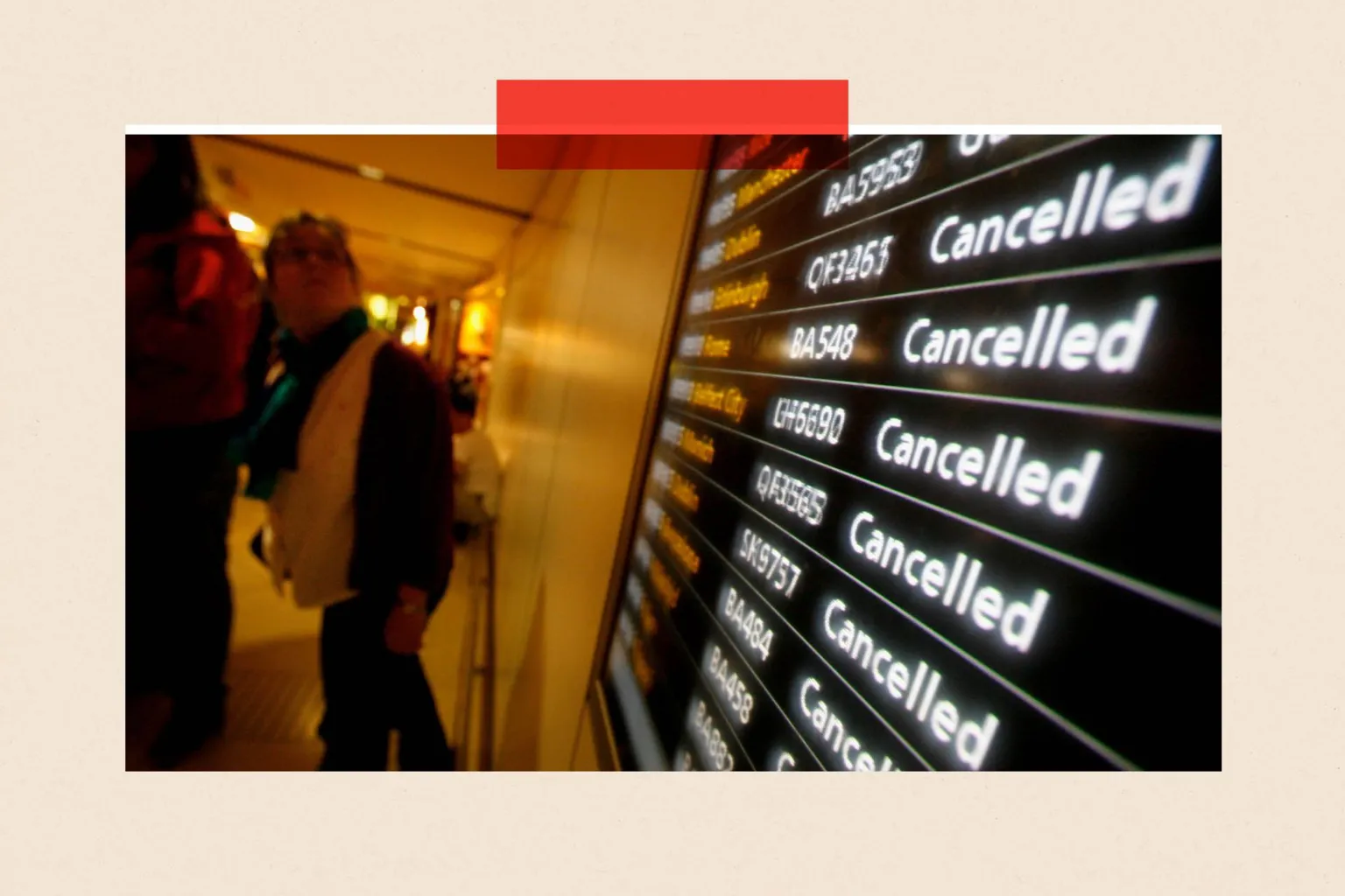  Wide-angle view inside an airport terminal showing a large electronic departures board on the right with multiple flight listings, each marked ‘Cancelled’ in bright white text against a dark background, with flight numbers visible. To the left, several travellers walk past the display along a softly lit corridor, with luggage and coats partially visible. The perspective emphasises the repeated cancellation notices.
