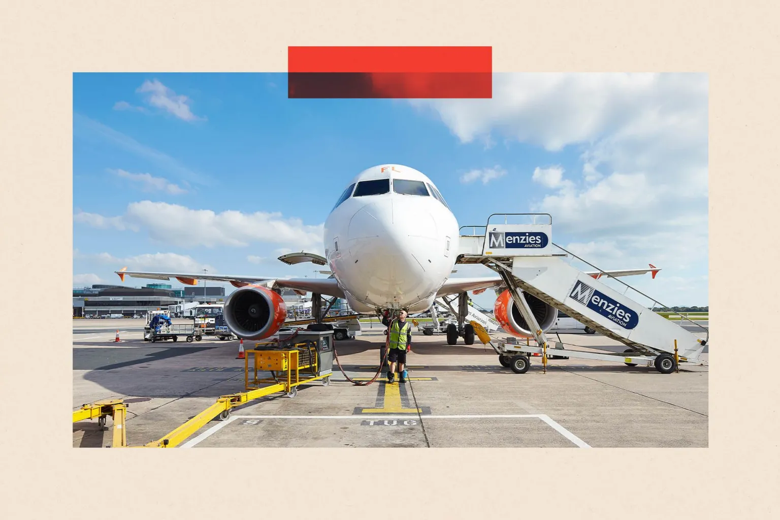 Front-on view of a parked commercial passenger jet, with ground crew working beneath the nose and a mobile staircase branded ‘Menzies Aviation’ positioned beside the aircraft. Service vehicles, equipment and terminal buildings are visible in the background under a blue sky with a few clouds.