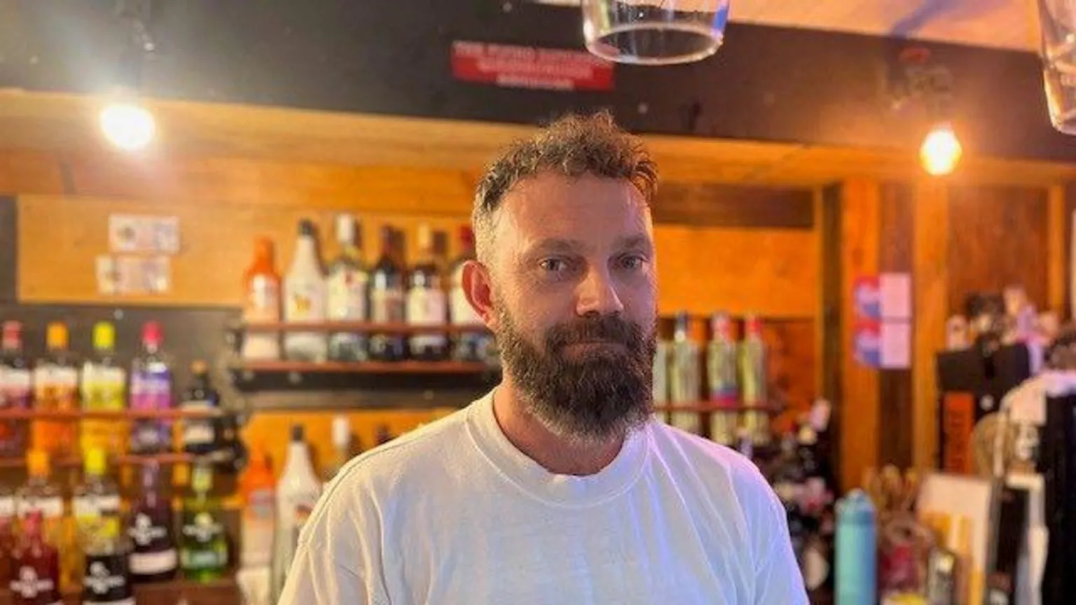 Matthew Nichol, who wears a white t-shirt and has a beard, looks at the camera inside The Flying Dutchman pub 