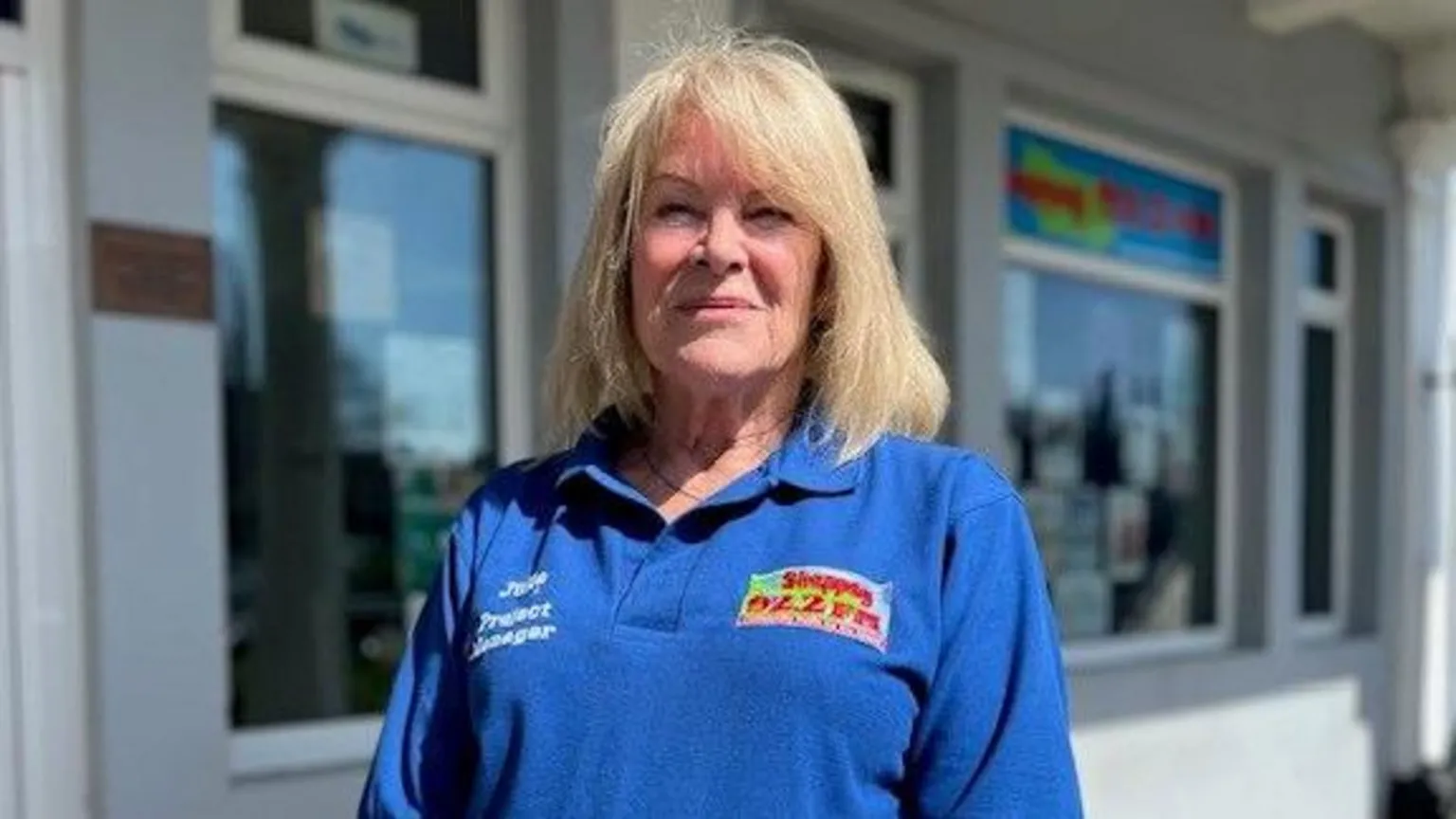 Julie Nicholls, who has shoulder-length blonde hair, smiles at the camera while wearing a blue Sheppey FM polo shirt.