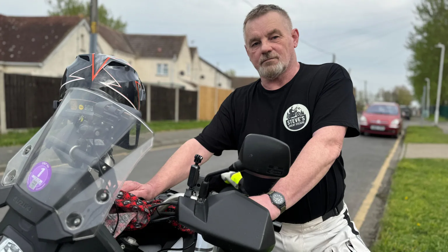 Steve Kilminster wears a black t-shirt and holds up his motorbike.
