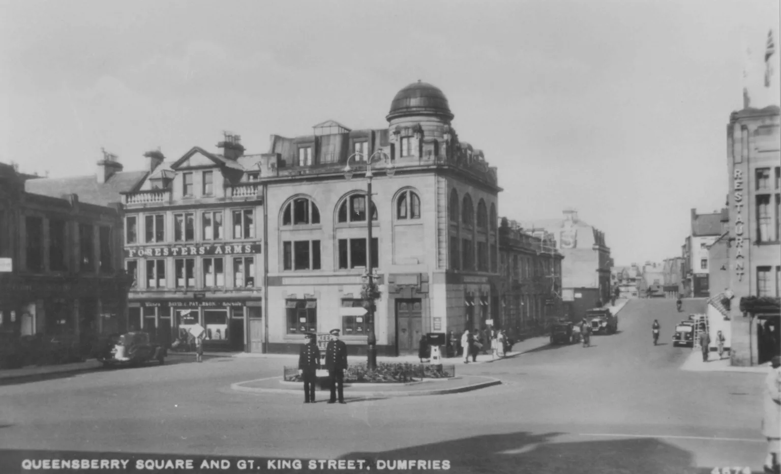 Heritage Service, Dumfries and Galloway Council A black and white picture of Queensberry Square and Great King Street in the centre of Dumfries. Wide open roads with just a handful of cars. Two policemen are standing in the middle of the square. 