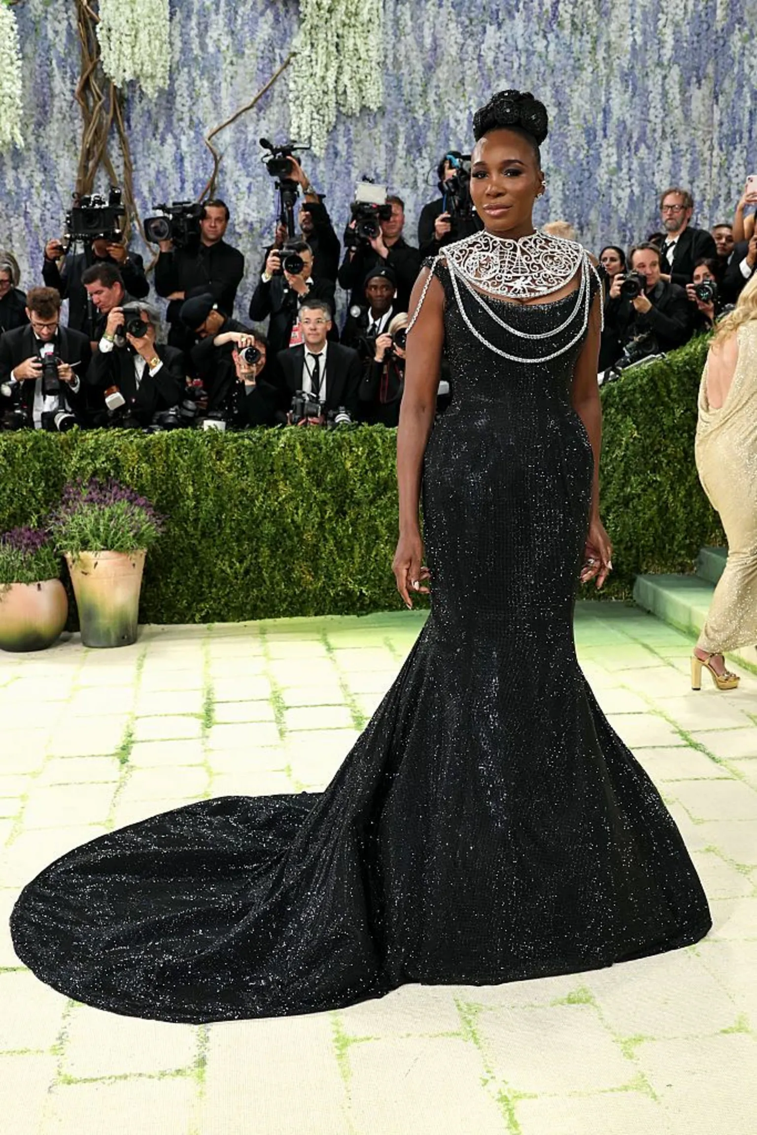  Venus Williams wears a black, sparkling gown with a flared train, but the star of the outfit is her large silver neck adornment.
