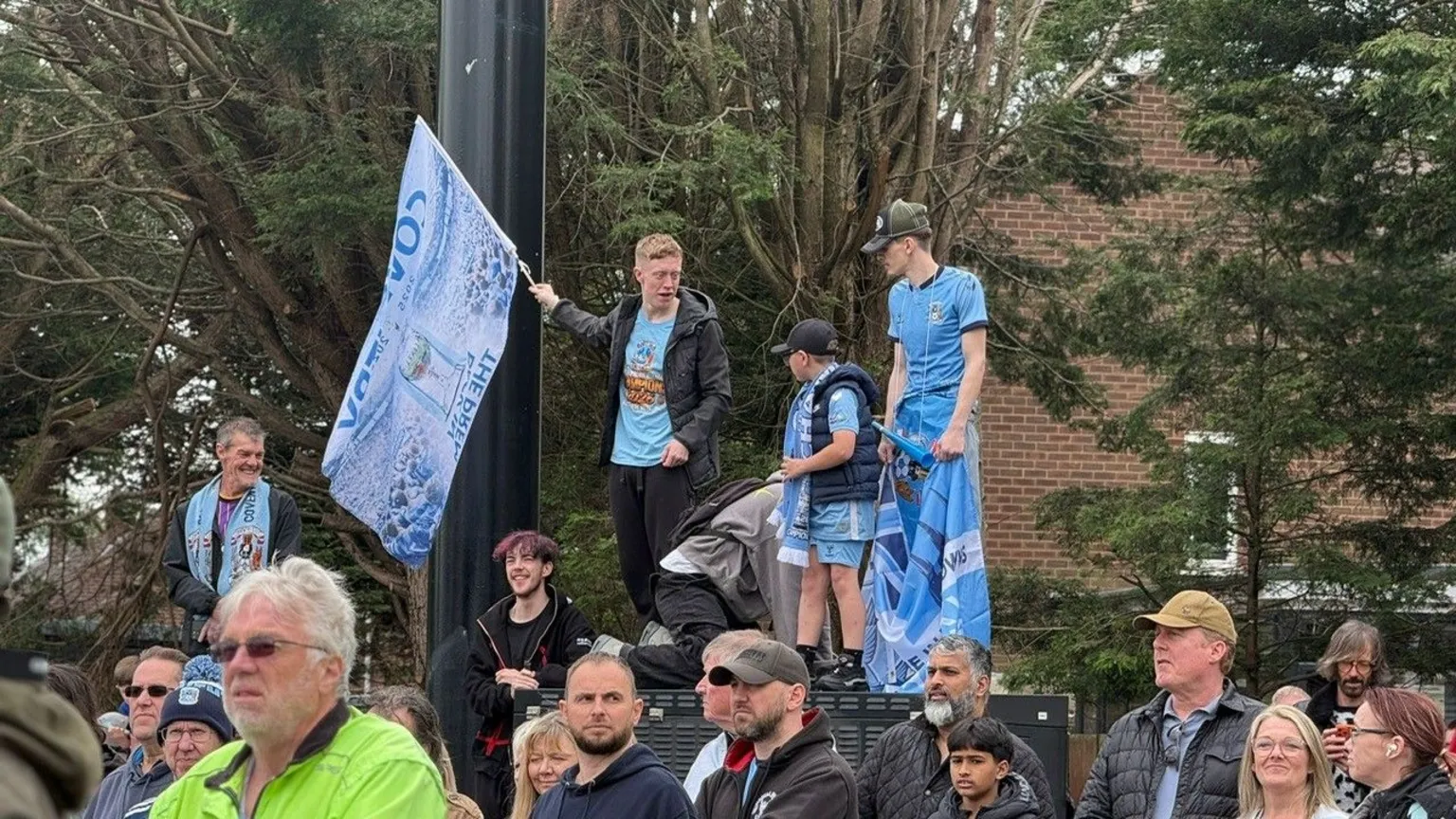 Fans standing on make-do platforms to get a better view. One is carrying a Coventry City flag