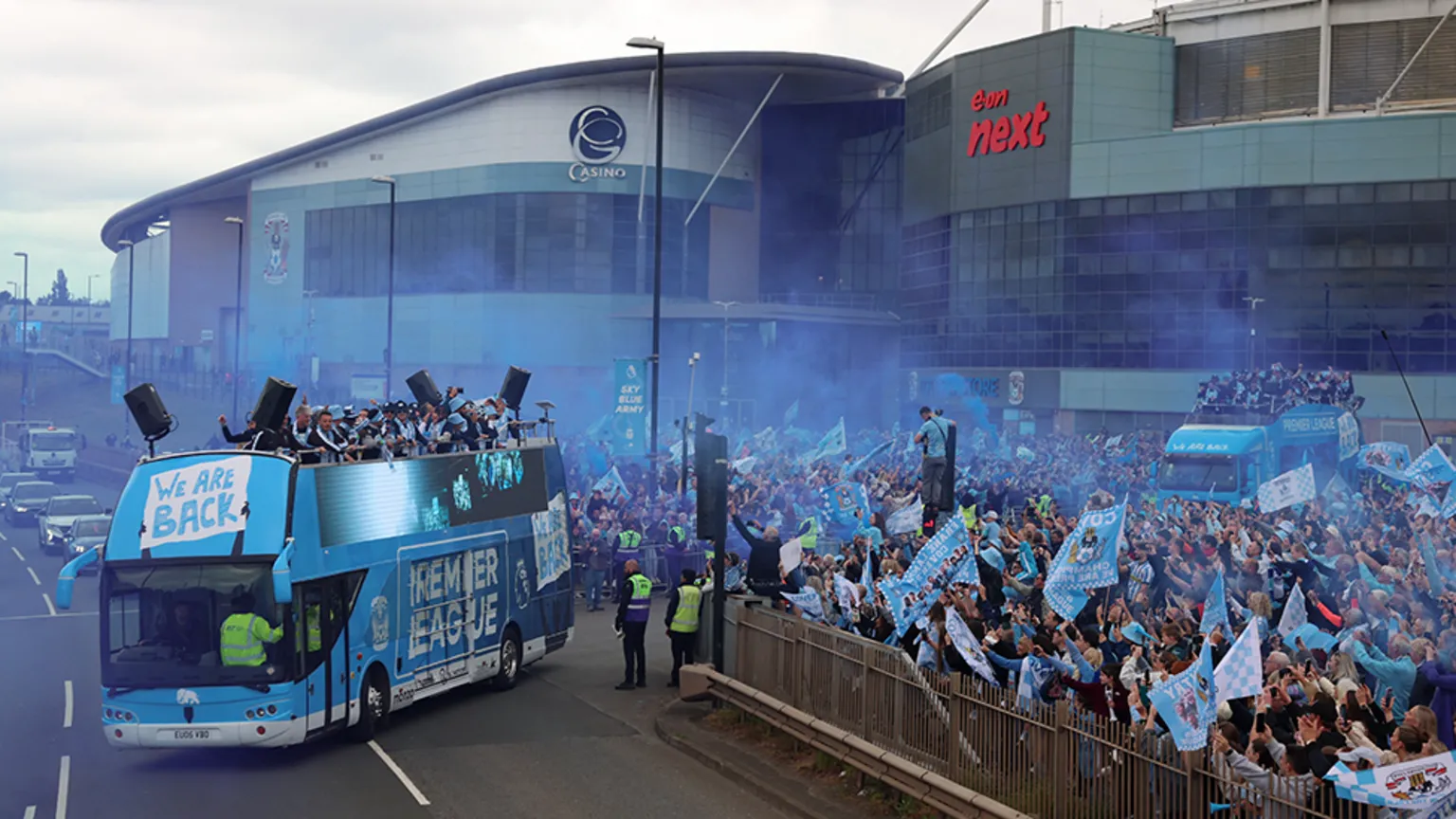  The bus leaving the CBS Arena with a large crowd behind fencing on the right