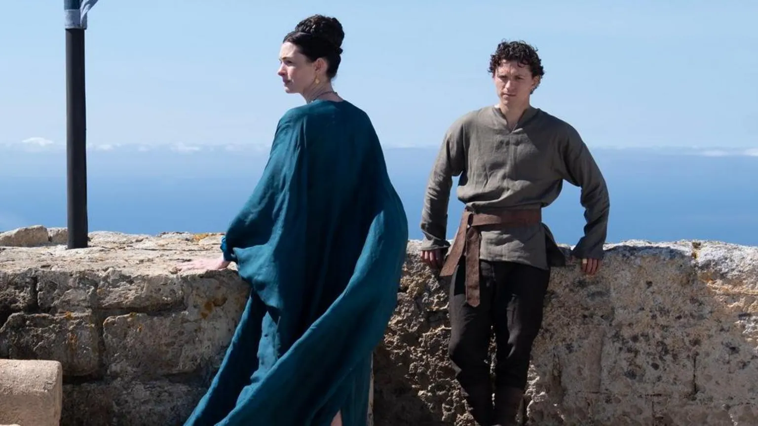 Universal Studios Anne Hathaway as Penelope and Tom Holland as Telemachus, together atop a castle overlooking the sea