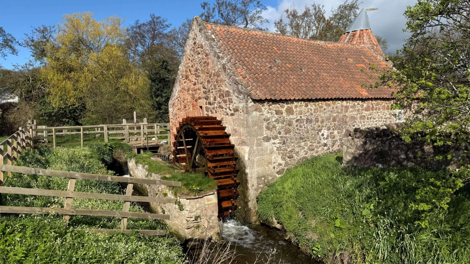  A waterwheel sits in a burn and is attached to a red brick building with a red tiled roof.