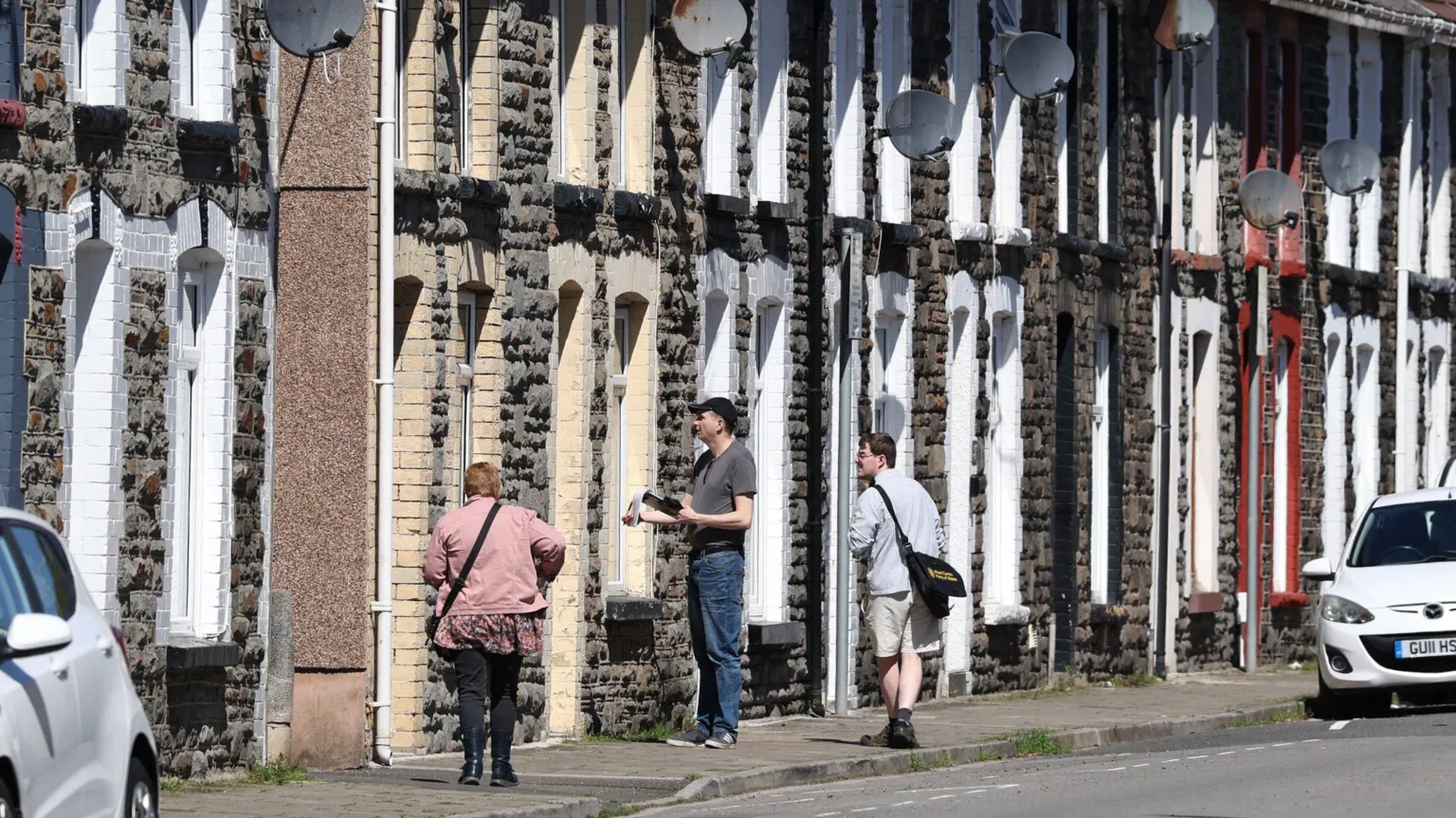  Three people canvass knock doors in a terraced street holding leaflets.