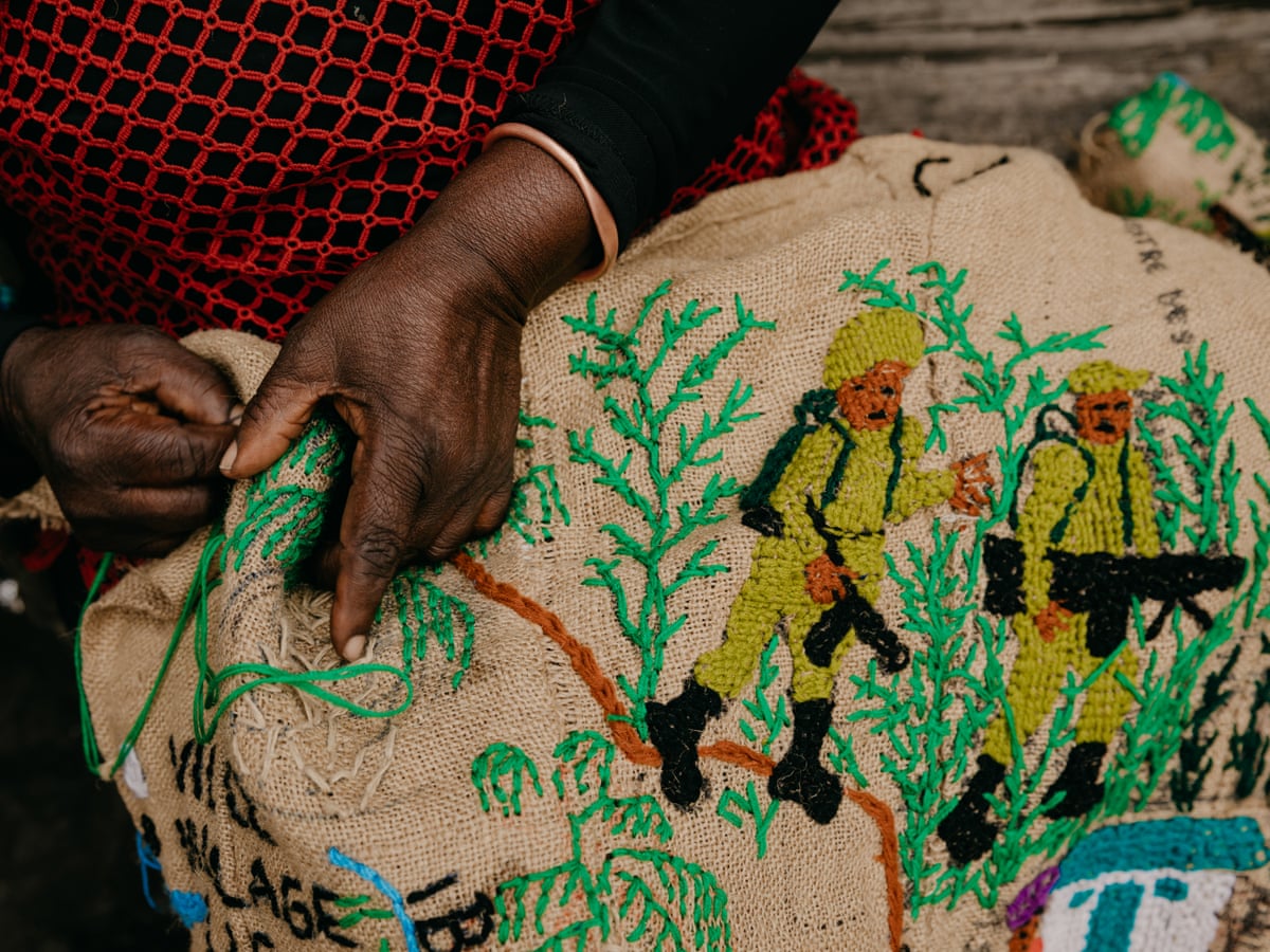 Detail of a woman’s hands stitching a scene of soldiers in the bush