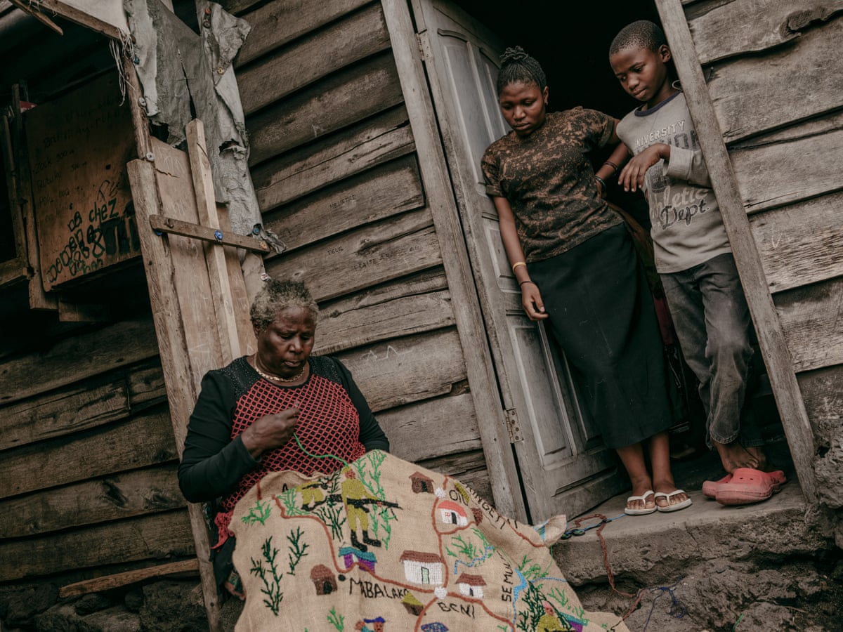 A woman and a boy stand in a doorway watching Kamusekera at work.