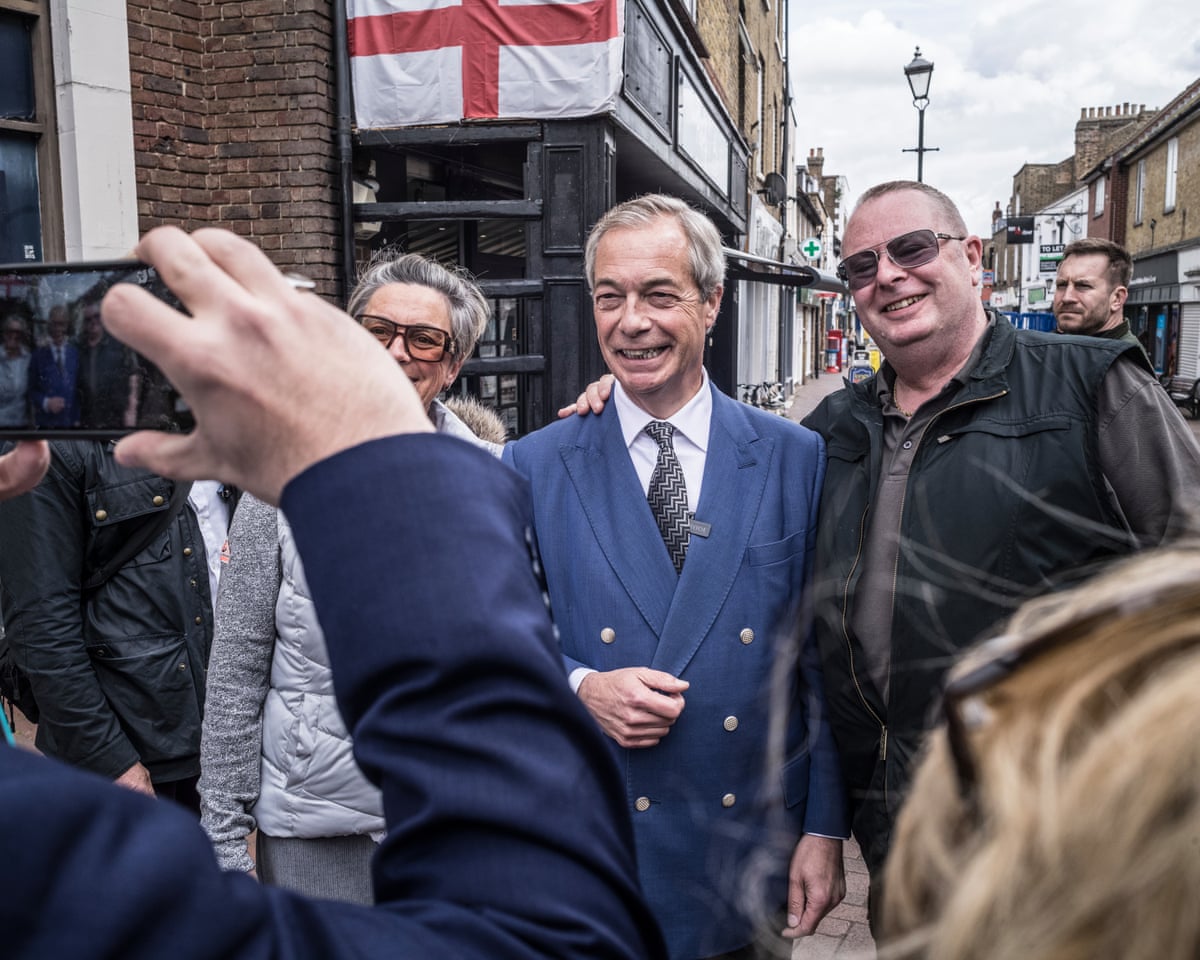 Nigel Farage poses for a photo with a smiling man with an English flag on a shopfront in the background