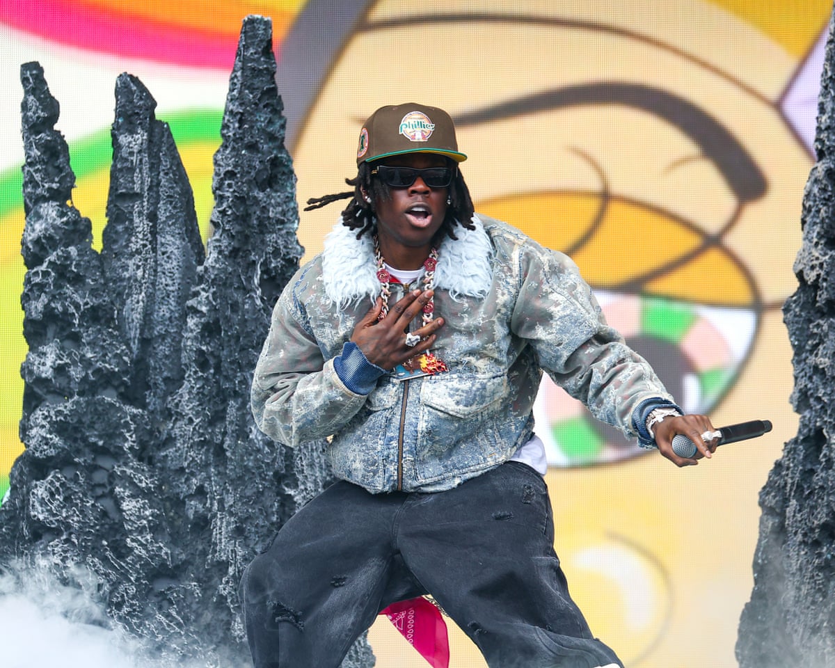 A man standing on stage holding a microphone with props and a colourful background behind him