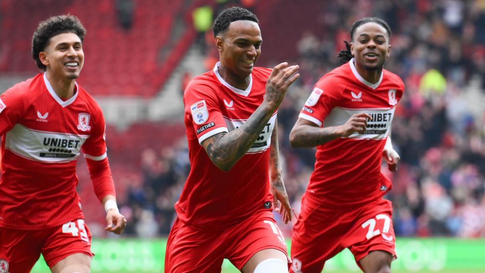 Morgan Whittaker, wearing Middlesbrough's red home shirt, smiles and runs as he celebrates a goal against Watford. His team-mates Jeremy Sarmiento and Sontje Hansen are running either side of Whittaker smiling.