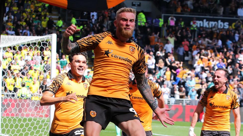 Oli McBurnie, wearing Hull City's amber and black home shirt, jumps in the air to celebrate the winning goal against Norwich City