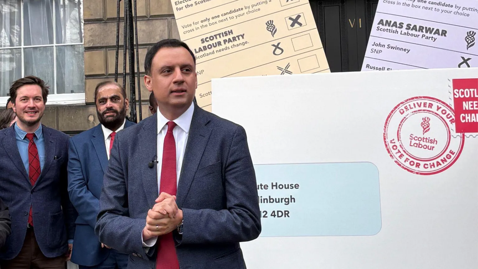  Anas Sarwar standing in front of a large white envelope and peach and lilac ballot papers outside Bute House in Edinburgh