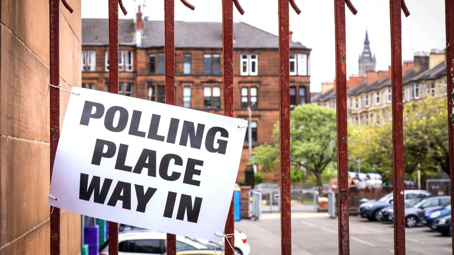  A polling place sign with black text on white paper attached to slightly rusted orange railings in Glasgow