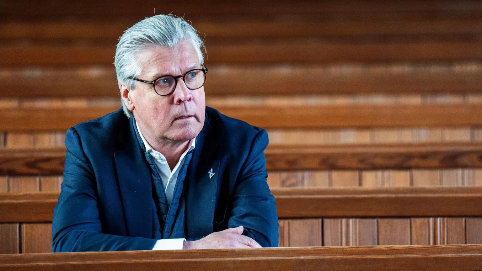  Malcolm Offord sitting on a church pew with his arms folded on top of the pew in front of him.