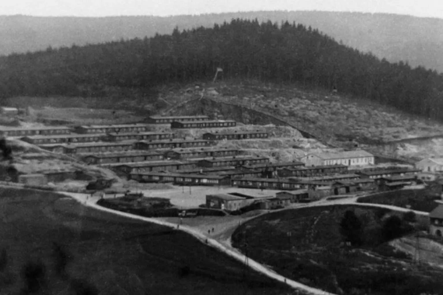 National Archive On a stark hillside are rows of long huts arranged in formidable structures, designed to prevent escape.