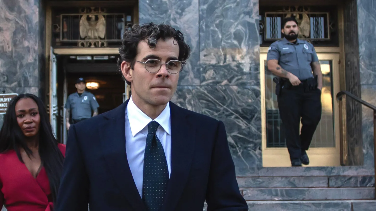 Adam Mosseri, with dark curly hair and glasses, in a dark suit, white shirt, and spotted tie, seen against the marble-façade and steps of the Los Angeles County Superior Court. 