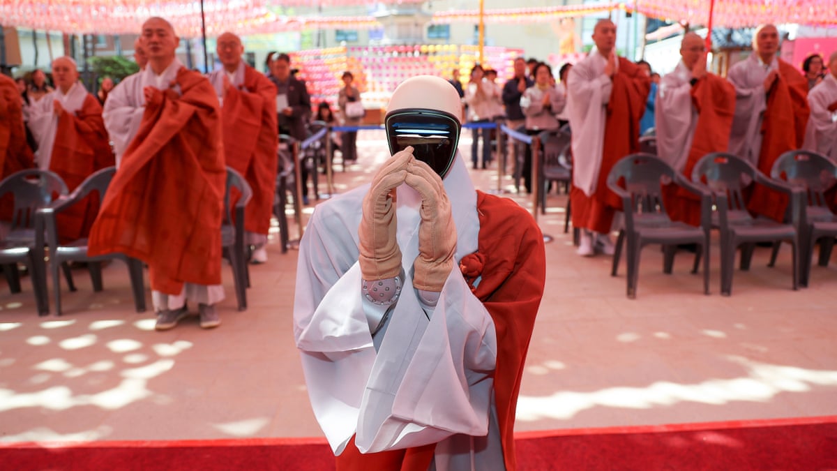 Humanoid robot puts its hands together with rows of monks behind it 
