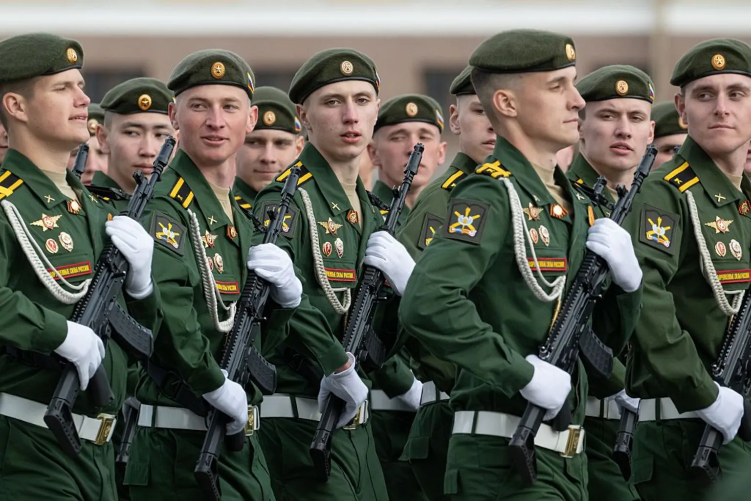  Russian soldiers rehearse for parade on Red Square - they are in uniform, holding automatic weapons with white gloves, marching left to right and looking towards the camera.