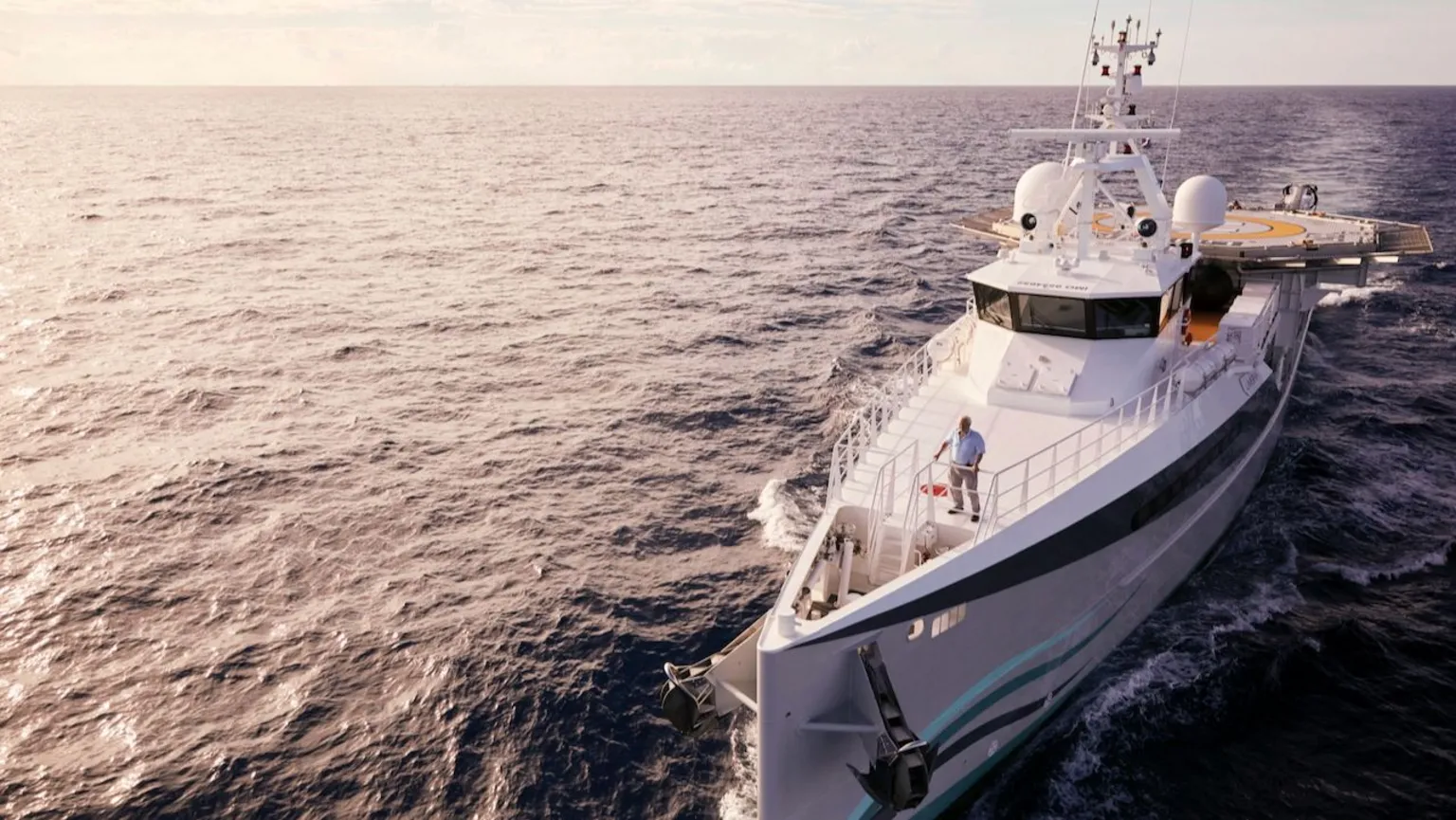 James Honeyborne A dramatic wide shot of Sir David Attenborough standing on the bow of a research vessel in the middle of the ocean on a sunny day