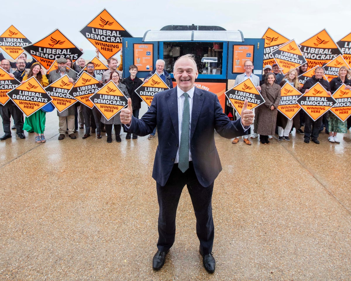 Happy Ed Davey in front of happy supporters with Lib Dem banners