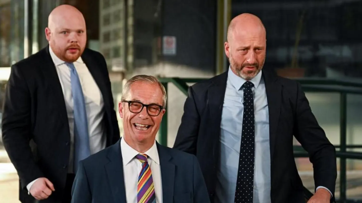  Britain's Reform UK leader Nigel Farage in glasses, a suit and stripey tie, followed by two men in suits, smiles as he leaves Millbank Tower
