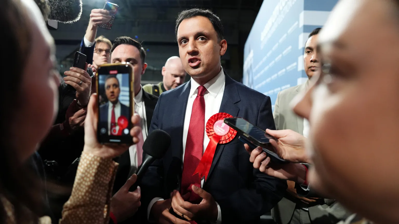  Anas Sarwar, in red tie with white shirt and dark suit, is surrounded by journalists with mics and phones. He is speaking.