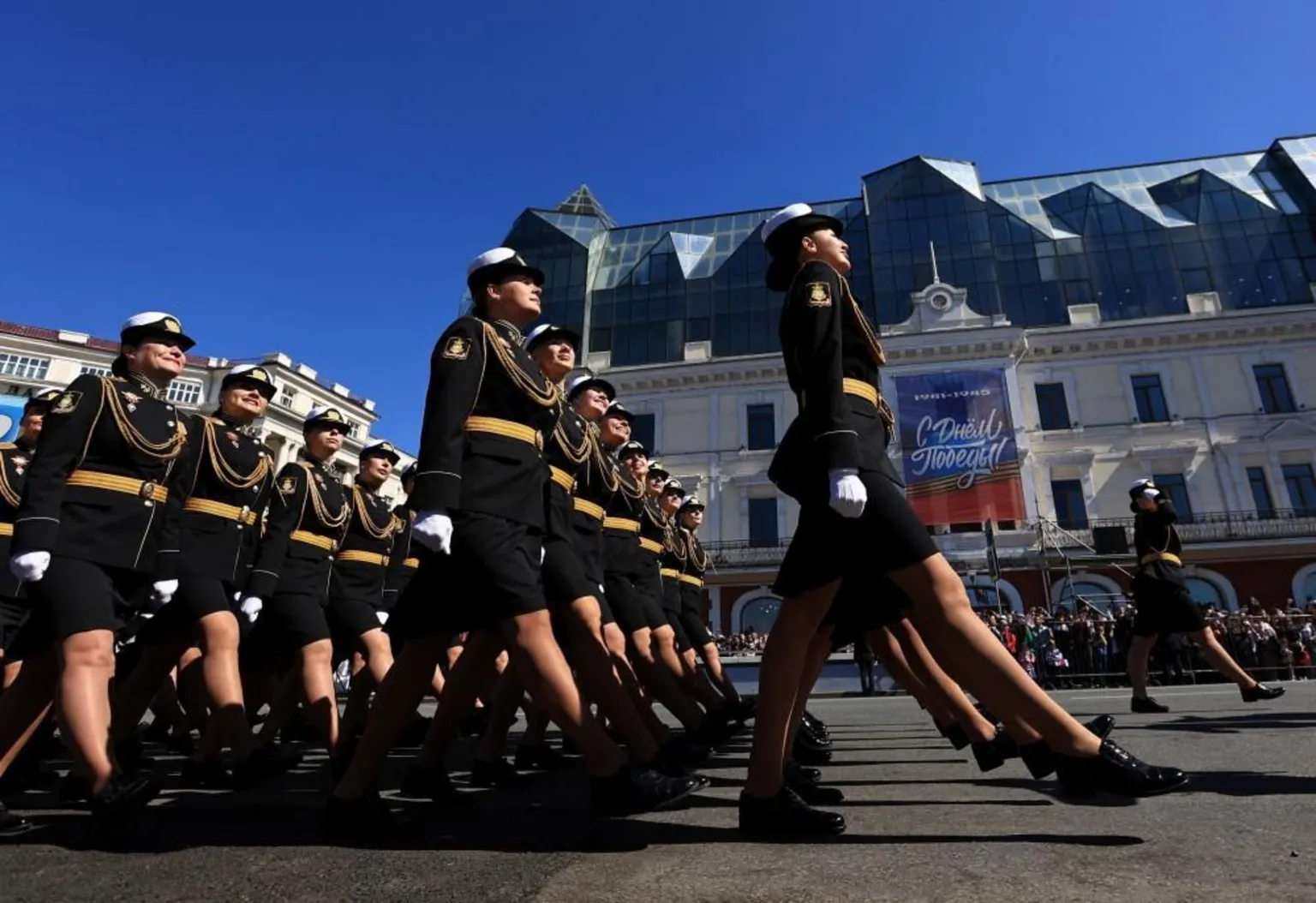  Russian service members march in rows along a road in Vladivostok. The regiment is made up of women wearing black and gold uniforms.