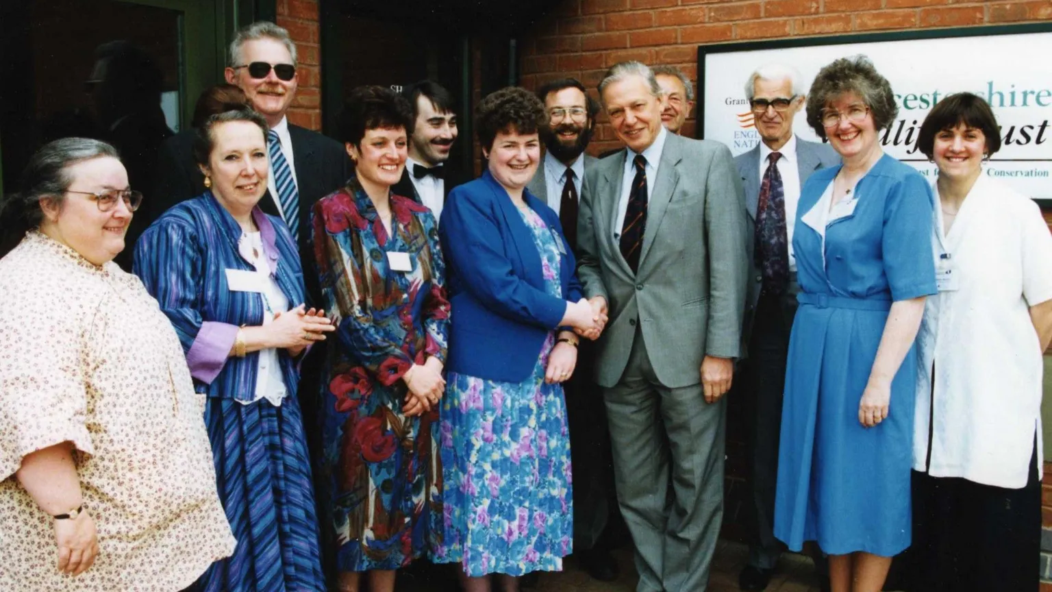 Gloucestershire Wildlife Trust A group of people stand with Sir David Attenborough at the opening of a conservation centre in the 1990s. They are wearing formal clothing and a woman with short hair is shaking Attenborough's hand.