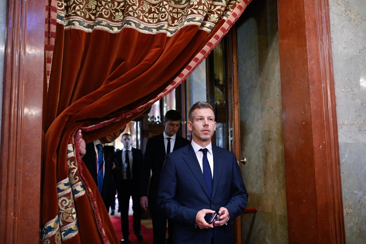 Péter Magyar stands next to a drawn-back red velvet curtain in Parliament. 