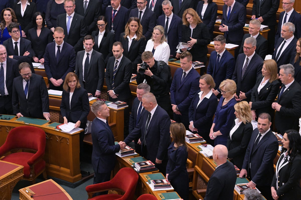Péter Magyar shakes the hand of a minister-elect in parliament as everyone looks toward him walking up the aisle. 