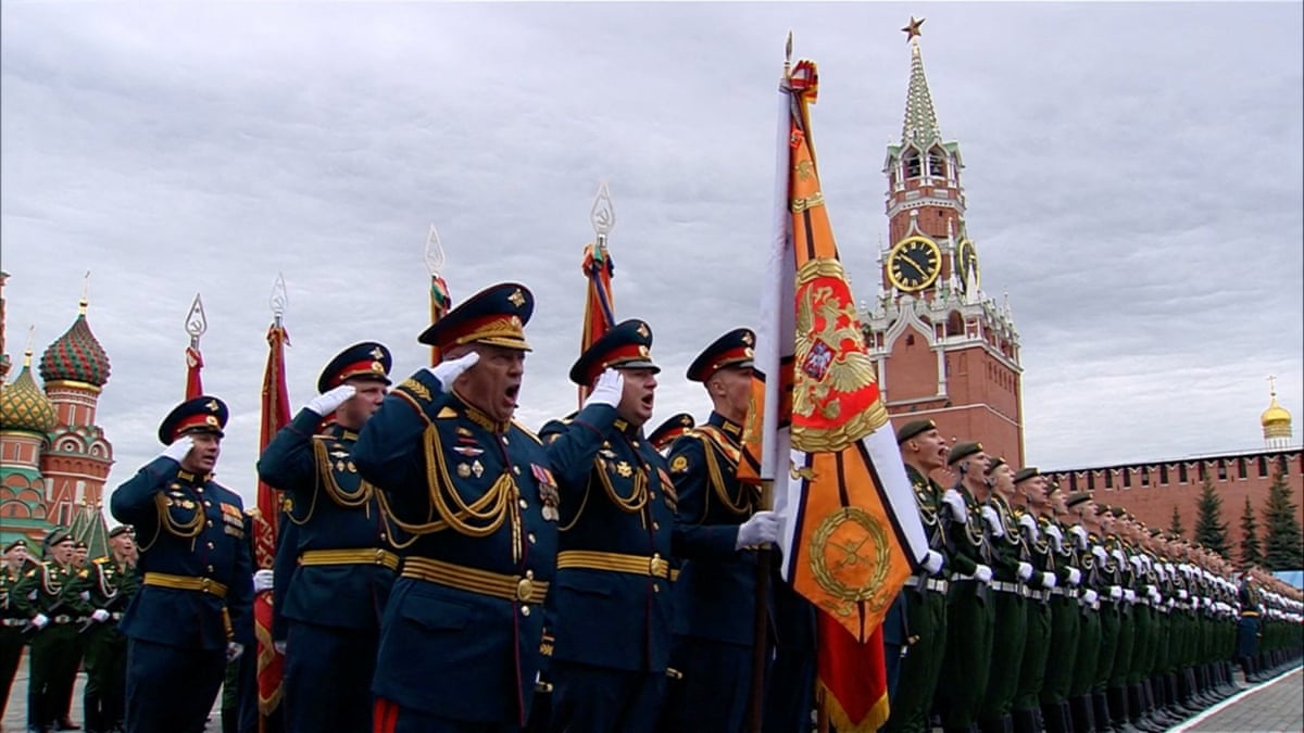 Some uniformed Russian service members stand in salute alongside other Russian service members in tidy lines in Moscow's Red Square under a cloudy gray sky. 