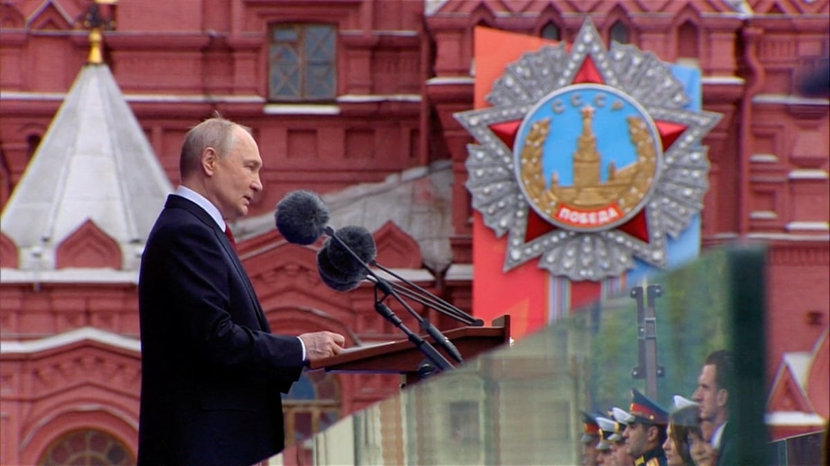 Vladimir Putin is photographed from the side standing at a podium, speaking into microphones, in Moscow's Red Square. 