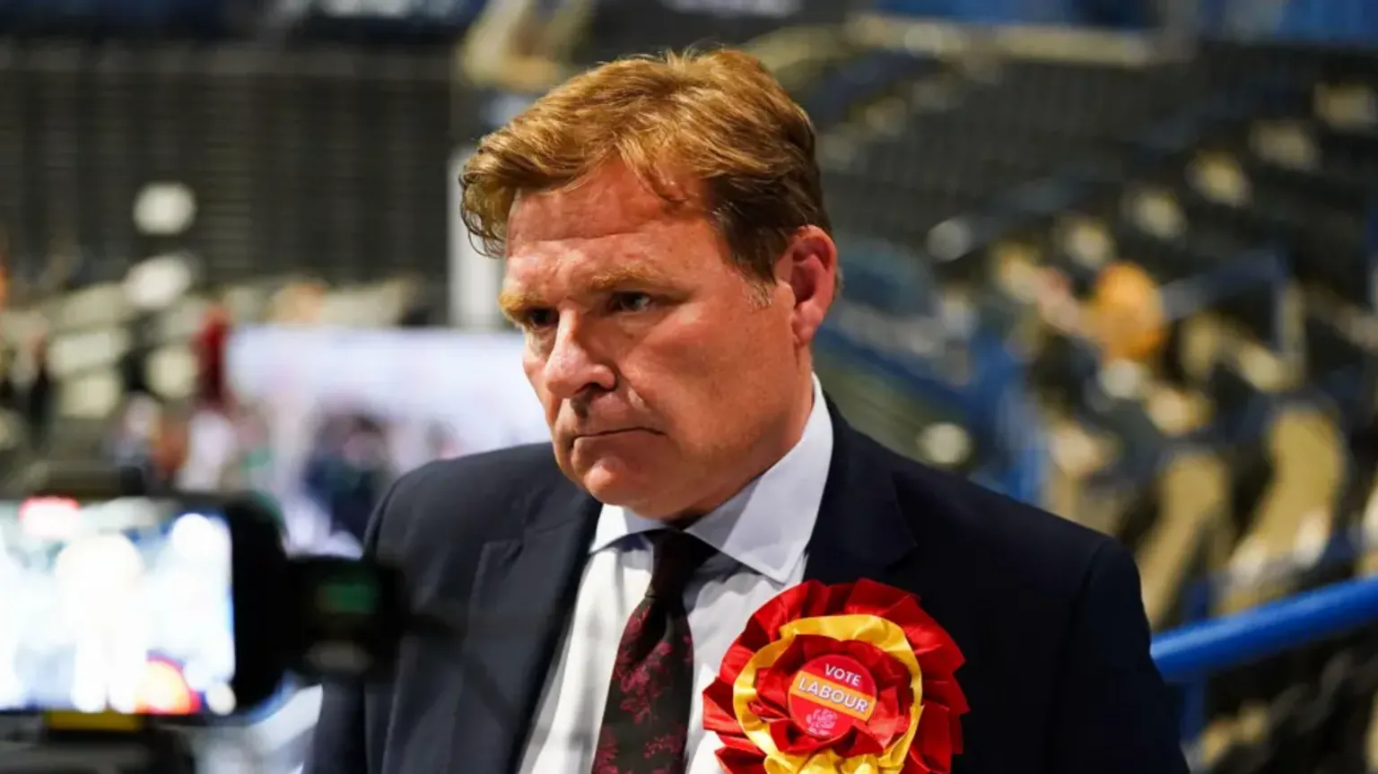 Jacob King/PA Wire A man with ginger hair looking solemn, wearing a red and yellow 'Vote Labour' rosette. 