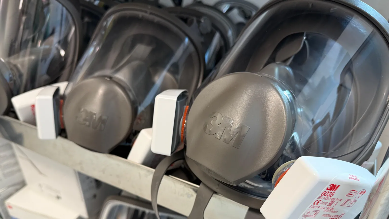 Two grey masks are displayed in a rack with clear panels for the face. 