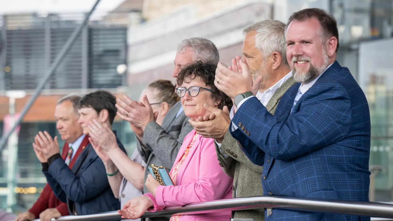 Rob Norman/Plaid Cymru A group of people stood next to each other clapping and smiling next to a railing