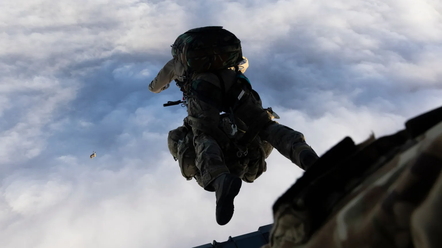 Ministry of Defence A paratrooper taking part in a parachute jump - they are seen having just left the plane and with the parachute pack on their back, with blue skies and clouds below them
