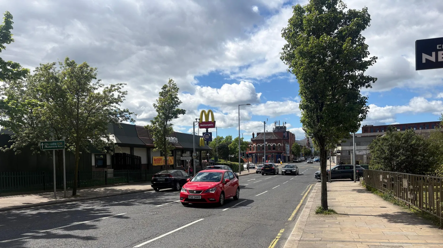 A road with cars driving on it. A McDonald's is on the left with trees lining the street.