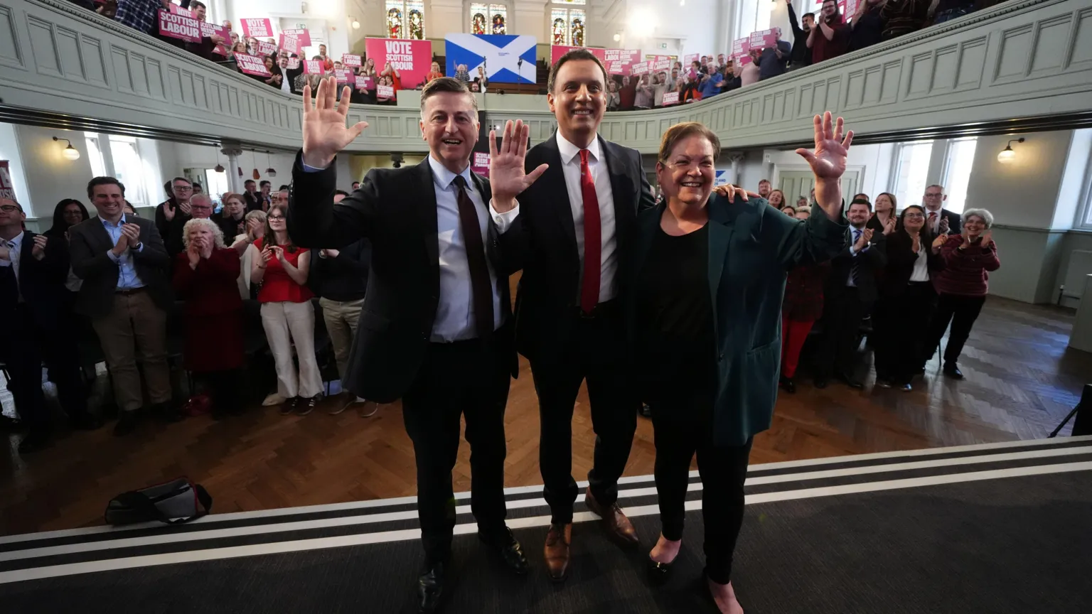  Scottish Labour leader Anas Sarwar, accompanied by Scottish Secretary Douglas Alexander (left) and deputy leader of the Scottish Labour Party, Dame Jackie Baillie, during an eve of poll rally at Adelaide Place Baptist Church in Glasgow, on the last day of campaigning ahead of the Holyrood elections on Thursday. They are in dark suits and are waving with a crowd behind them.