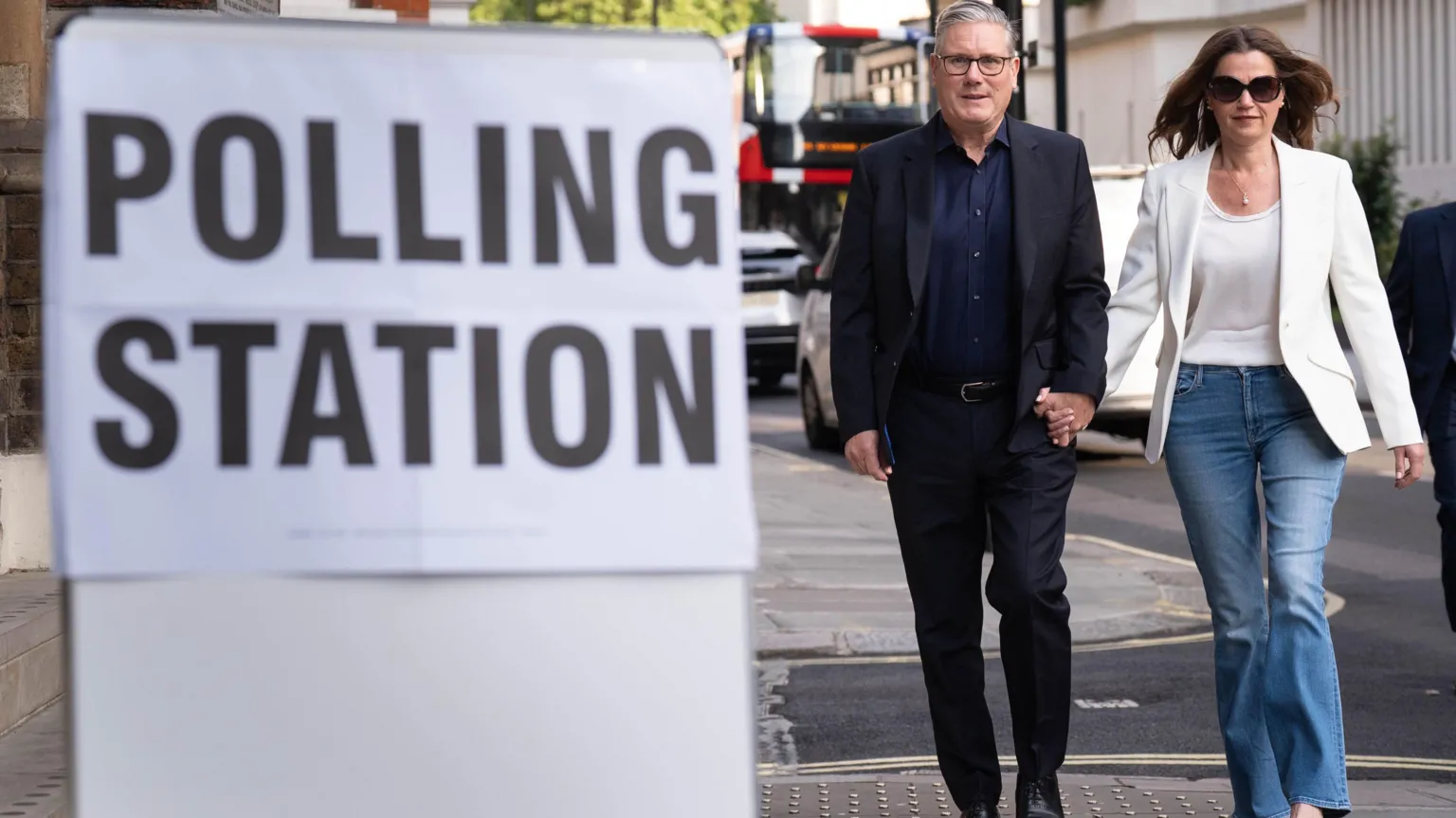  Labour leader Sir Keir Starmer and his wife Lady Victoria Starmer arrive to cast their votes in the local elections at Westminster Chapel in central London. He is in a dark suit and dark blue open-necked shirt. She is in a white jacket, white blouse, and jeans. They are holding hands.
