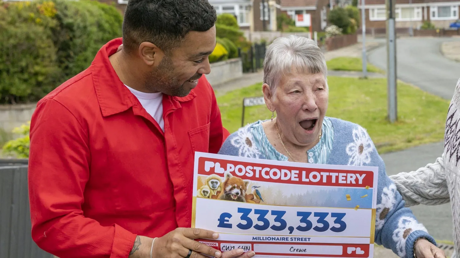 Postcode Lottery A man in a red shirt hands Nancy her cheque. She looks stunned with her mouth wide open in shock.