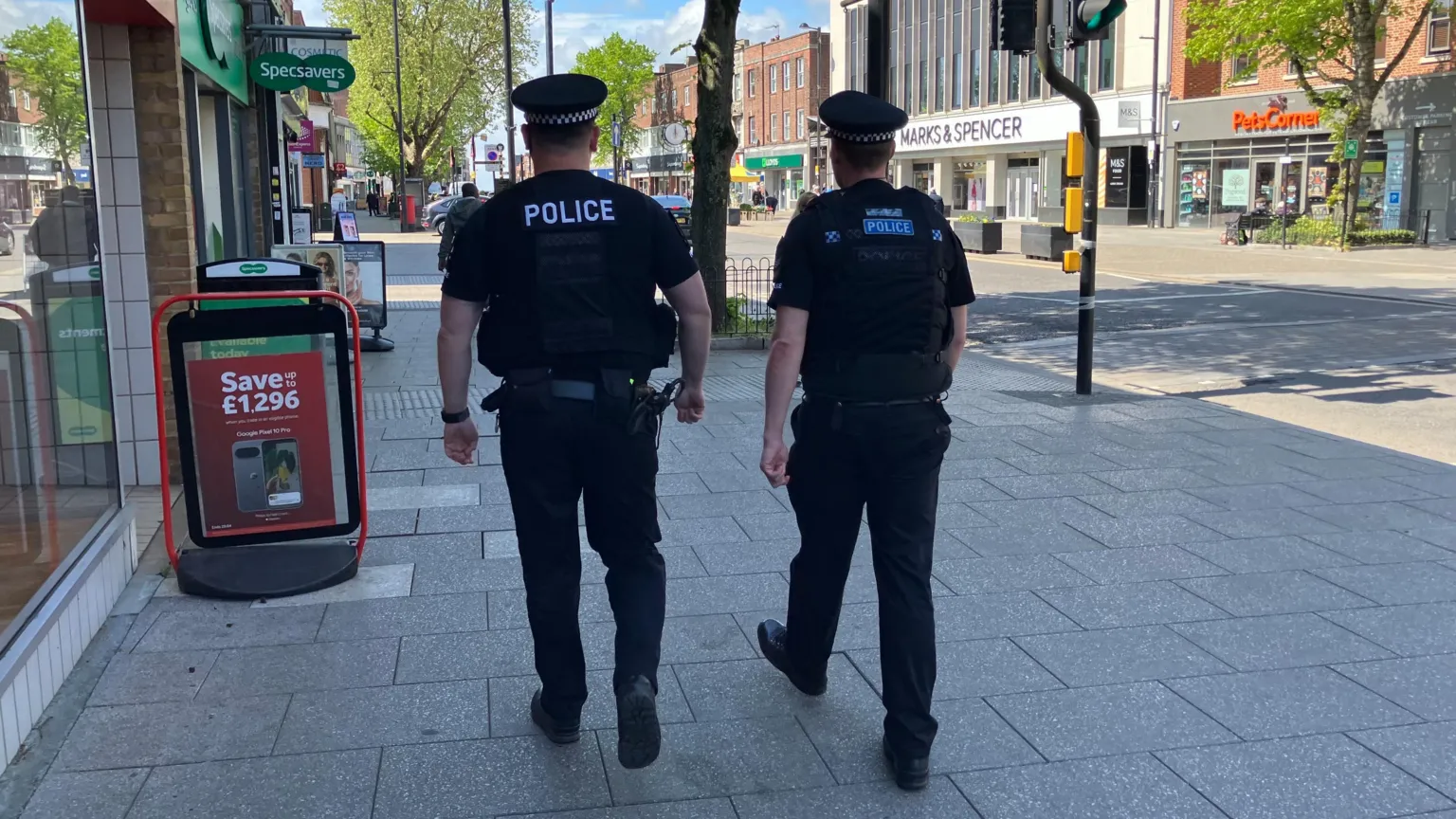 Rear view of two police officers on patrol in a High Street, with Marks and Spencer and Specsavers stores