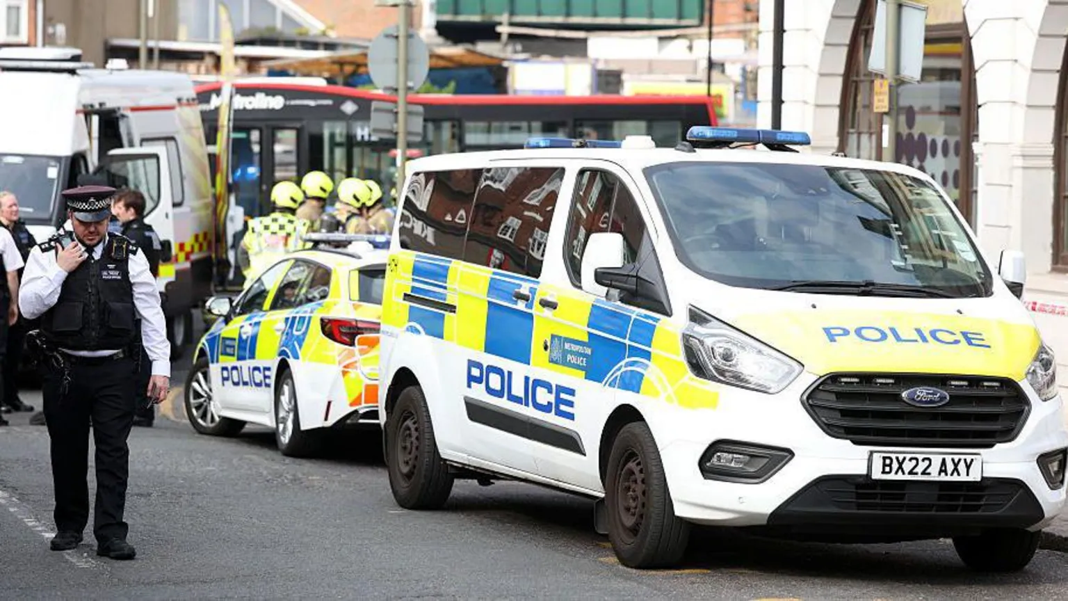 A policeman standing in front of a police van and police car