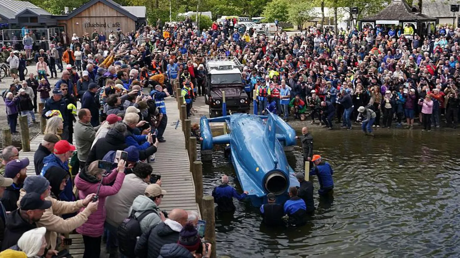  Bluebird is gently lowered into the water backwards. Hundreds of people are gathered closely by and taking pictures on their mobile phones.