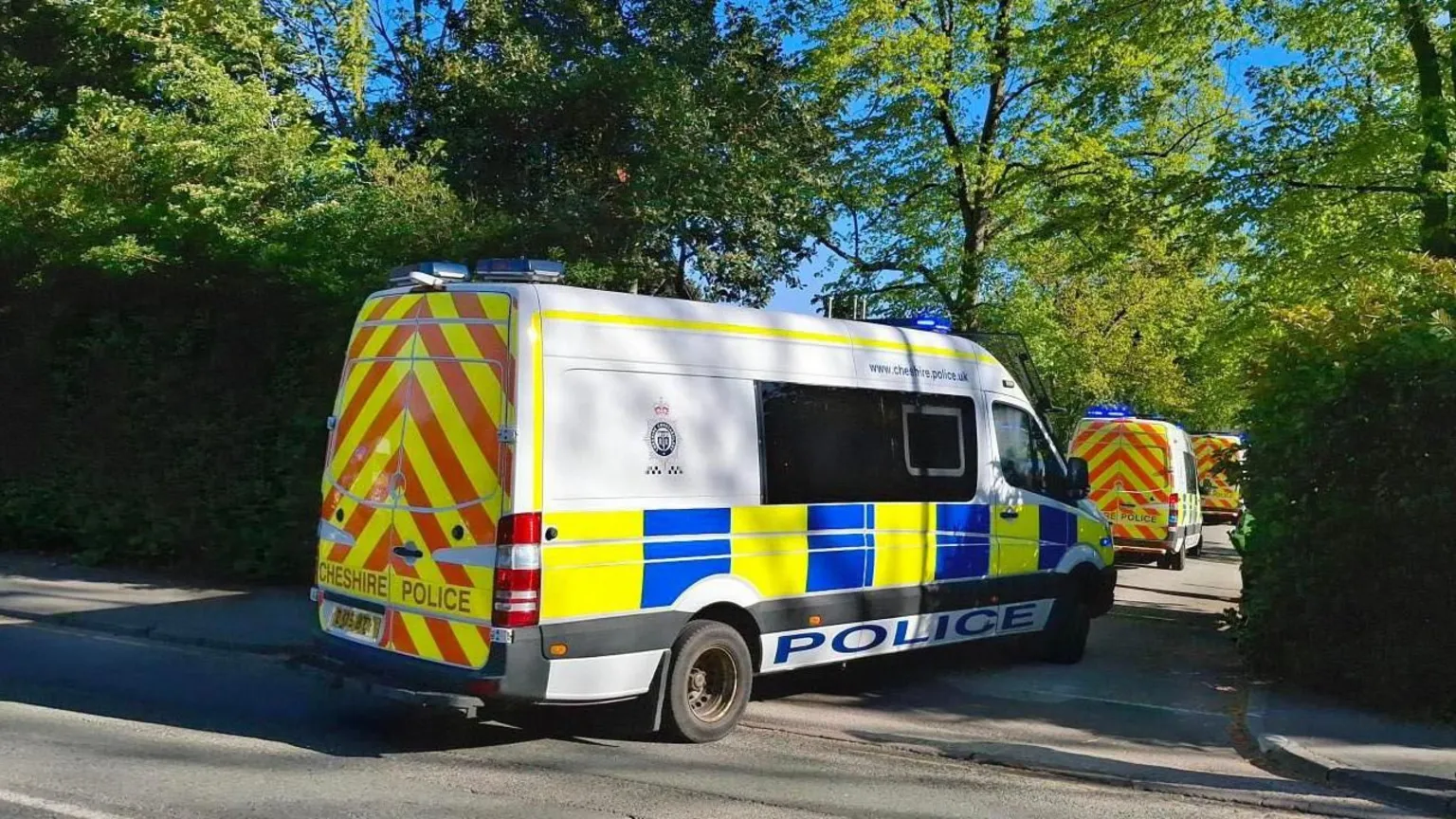 Cheshire Police Three police vans in a row, parked in a a small side road. There are trees either side of the road.