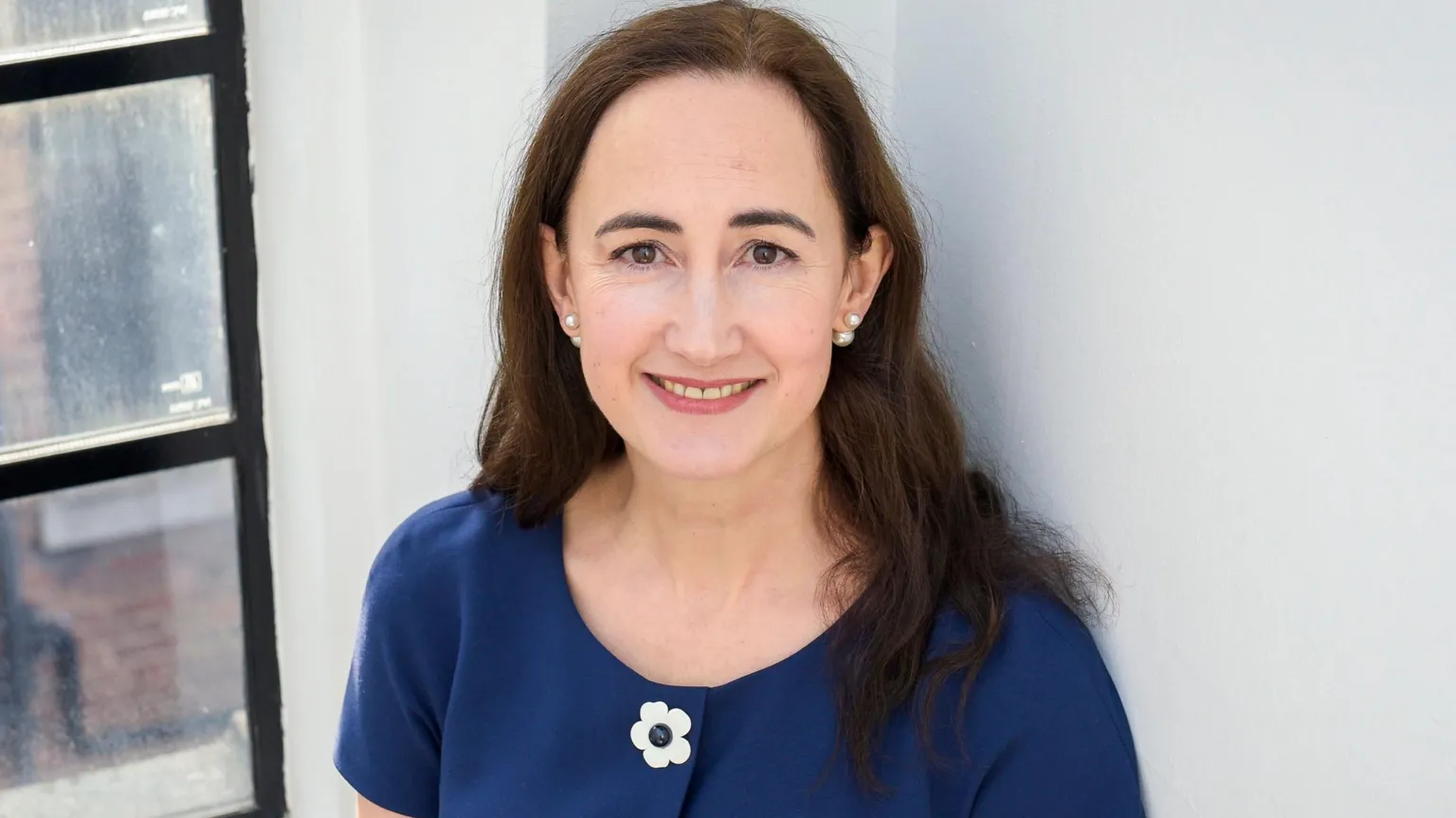 Sophie Kinsella pictured in 2018, standing against a white wall and window